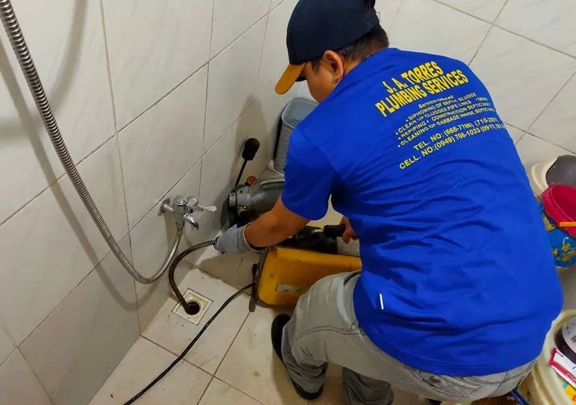Plumber using a drain snake machine on a bathroom floor drain.