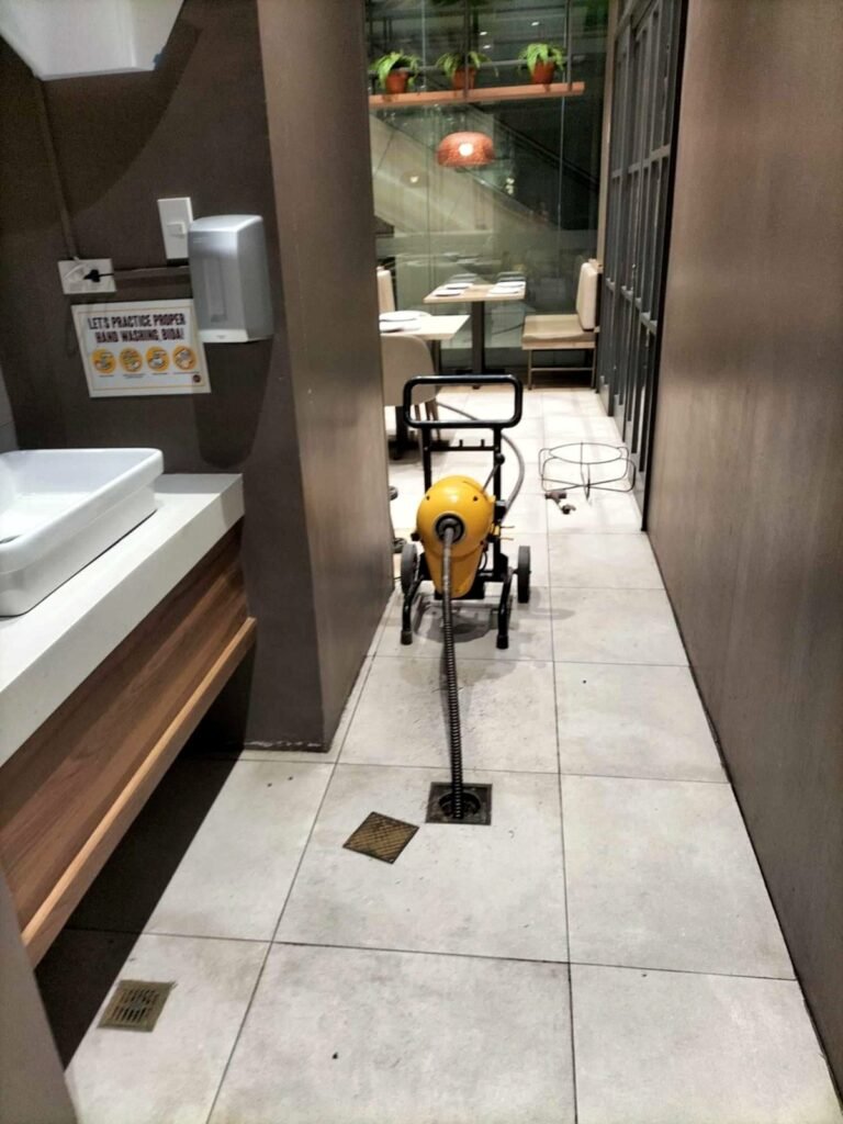 Electric drain cleaning machine clearing a floor drain in a commercial restroom